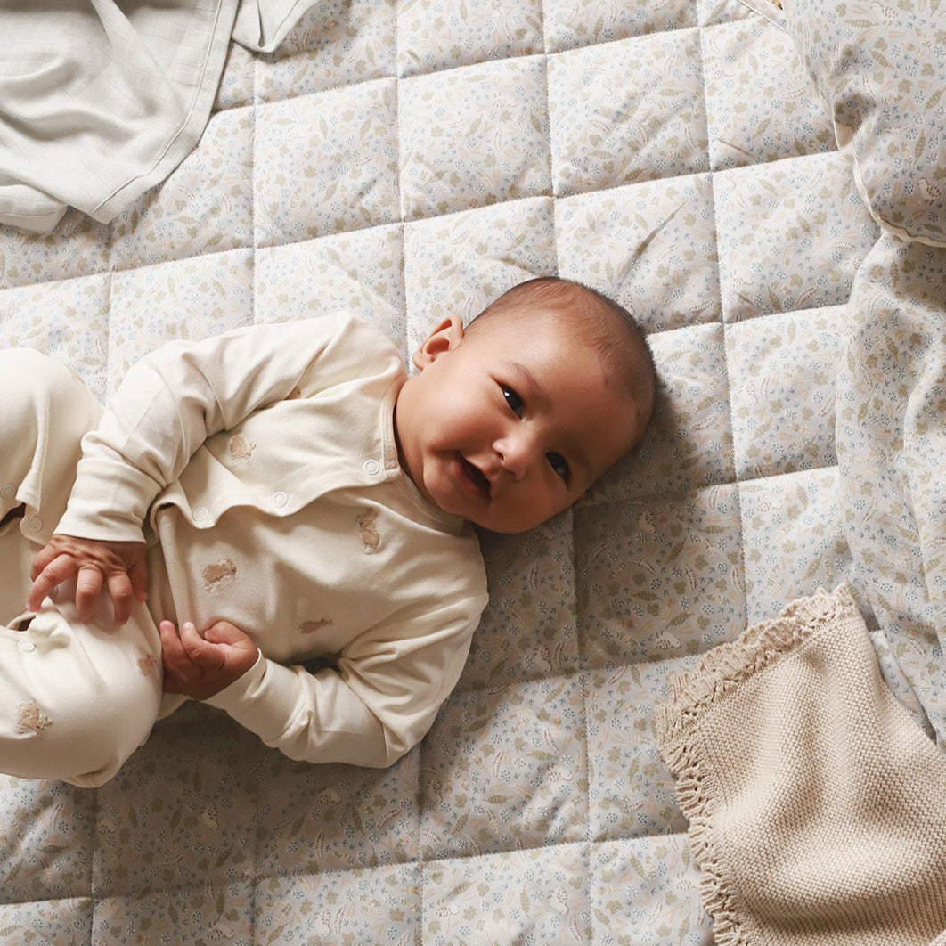 A baby smiling while lying on a playmat nature trail