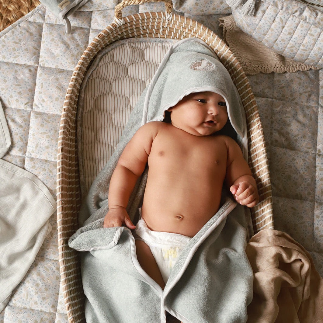 A baby wearing a hooded towel lying on a changing basket with cotton liner in nature print design