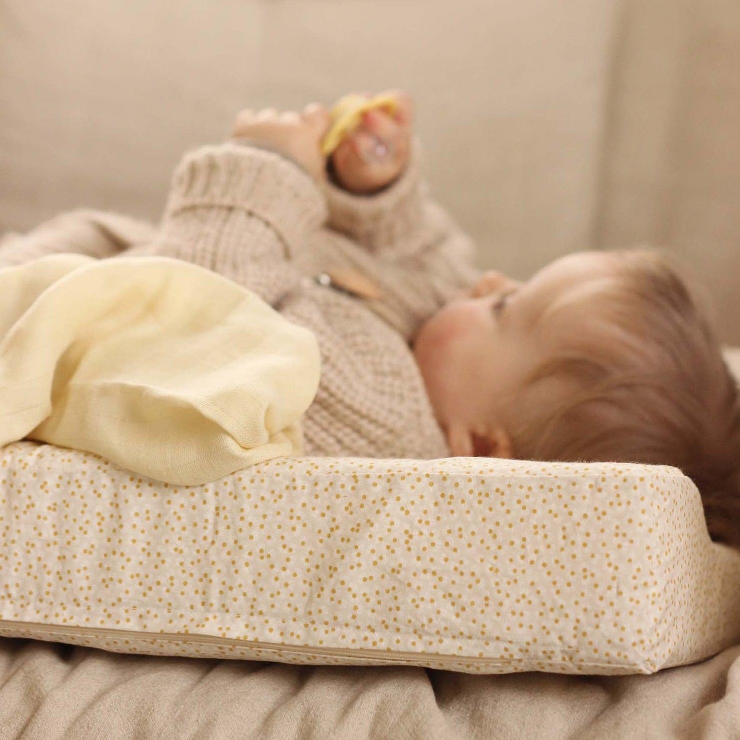 A baby playing with a teether while lying on a changing cushion with daisy meadow cover