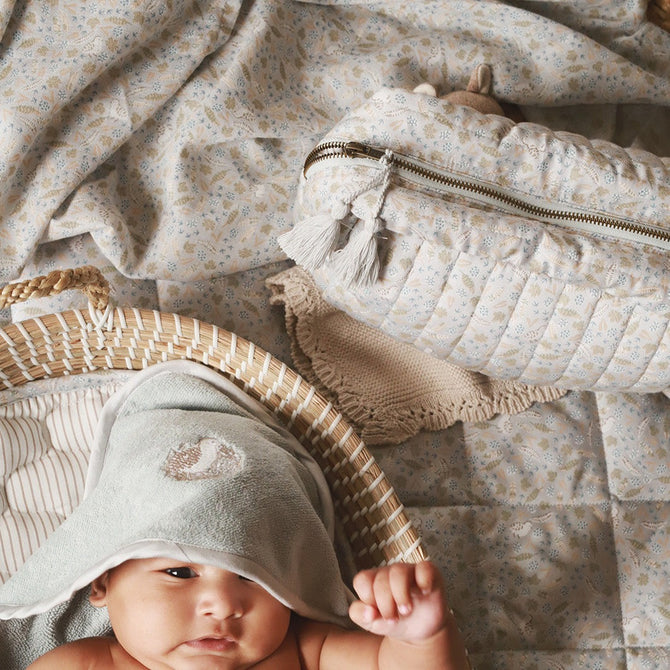 A baby wearing a hooded towel in quail design with wash bag nature trail beside