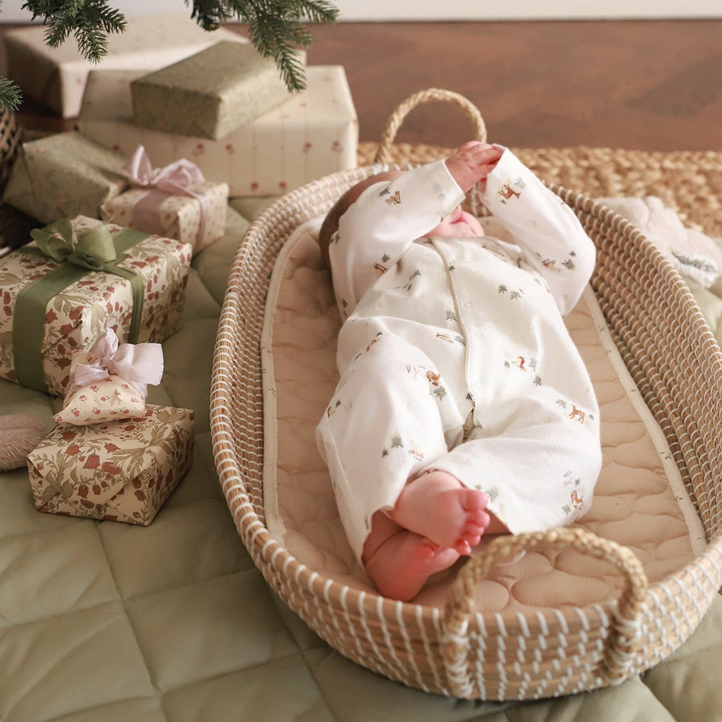A baby wearing a sleepsuit in winter ski design lying on a changing basket next to Christmas gifts