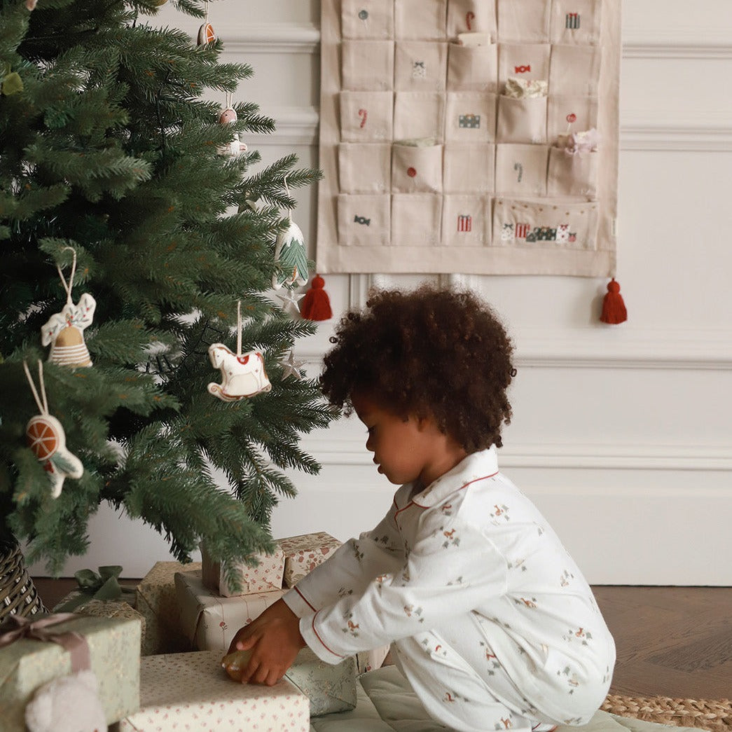 A boy wearing a nutcracker pyjamas sitting under the Christmas tree