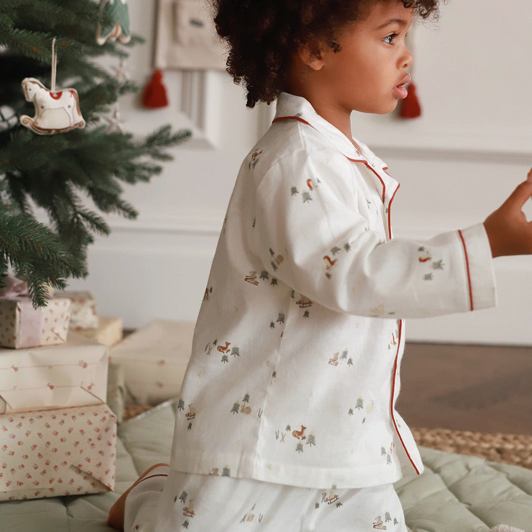 A boy wearing a nutcracker pyjamas standing next to gifts