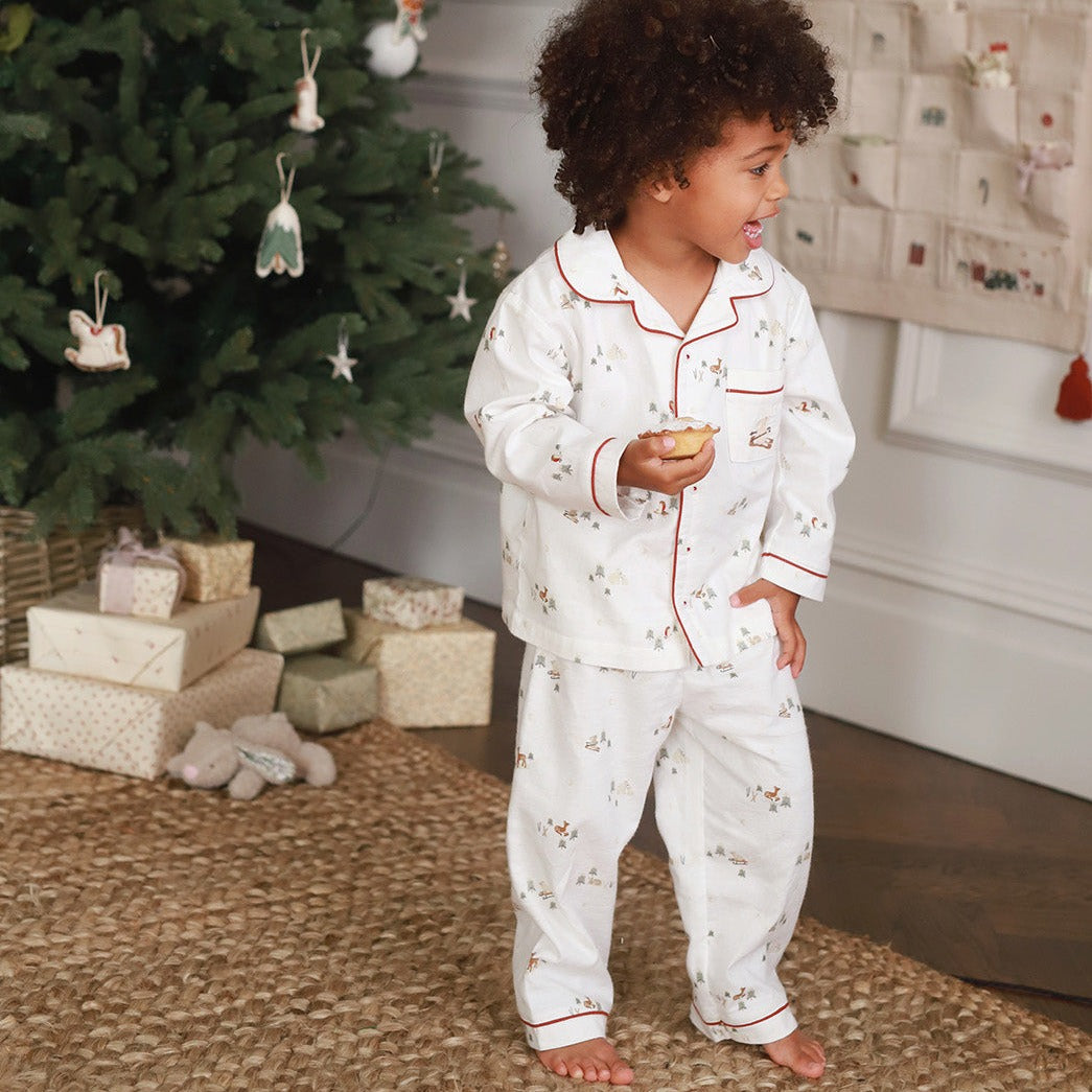 A boy wearing a nutcracker pyjamas while holding a muffin