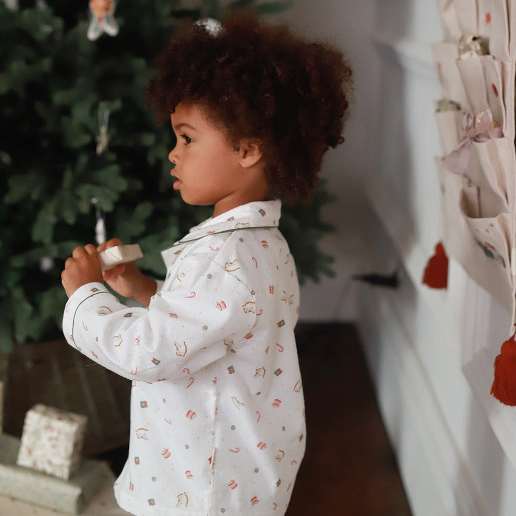 A boy wearing a nutcracker pyjamas while holding a small Christmas present