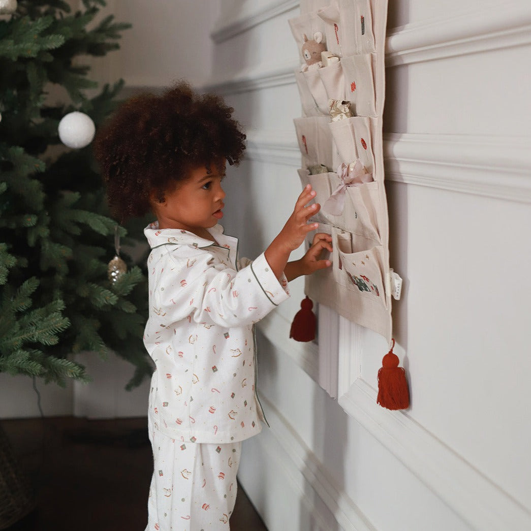 A boy wearing a nutcracker pyjamas while standing next to advent calendar