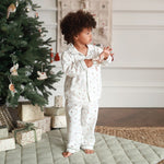 A boy wearing a nutcracker pyjamas while standing next to Christmas tree