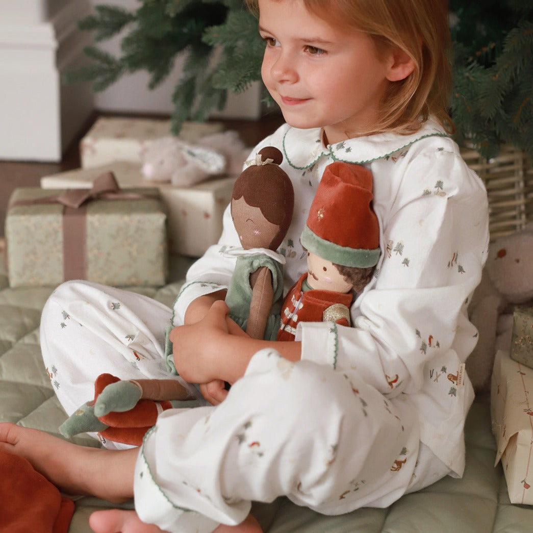 A girl holding two Christmas dolls while seated under the Christmas tree