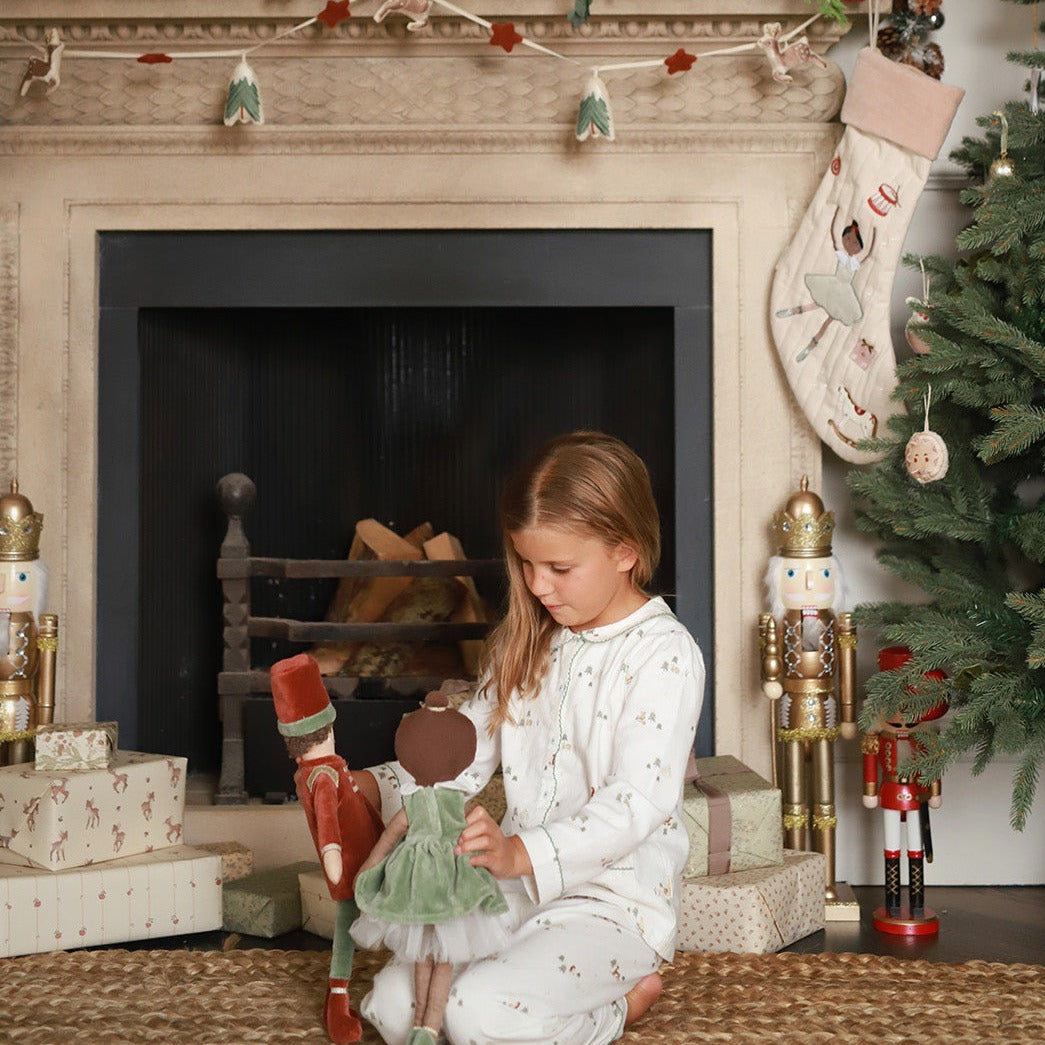 A girl playing with ballerina doll and nutcracker doll near the chimney