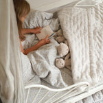 A girl reading on a cotbed bedding set nature trail design