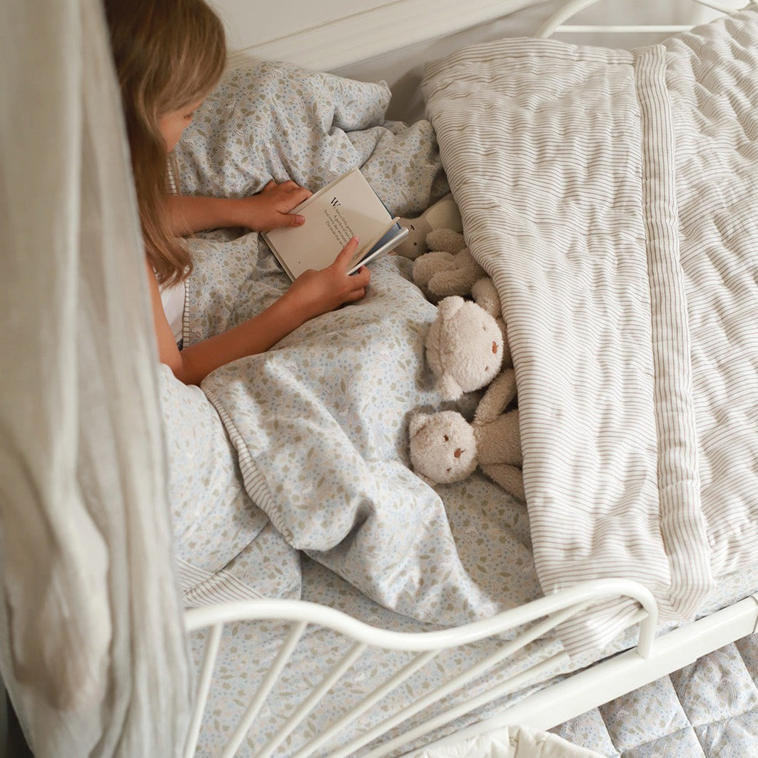 A girl reading on a quilted bedspread in natural stripe