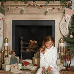 A girl sitting next to the chimney with Christmas stocking and unboxing Christmas gift