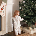 A girl wearing a nutcracker pyjamas standing between the Christmas tree and christmas stocking