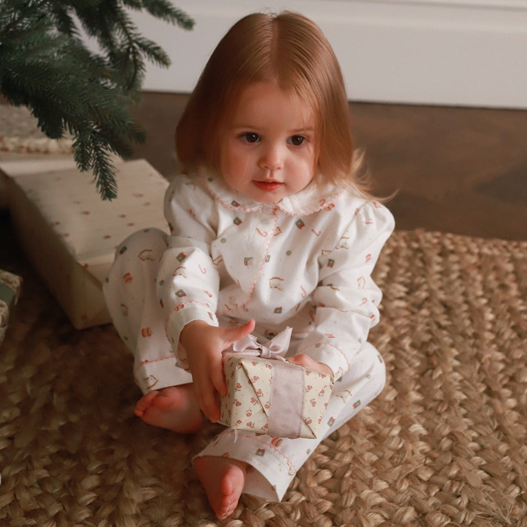 A girl wearing a nutcracker pyjamas while sitting under the Christmas tree