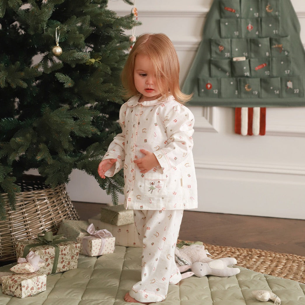 A girl wearing a nutcracker pyjamas while standing next to Christmas tree