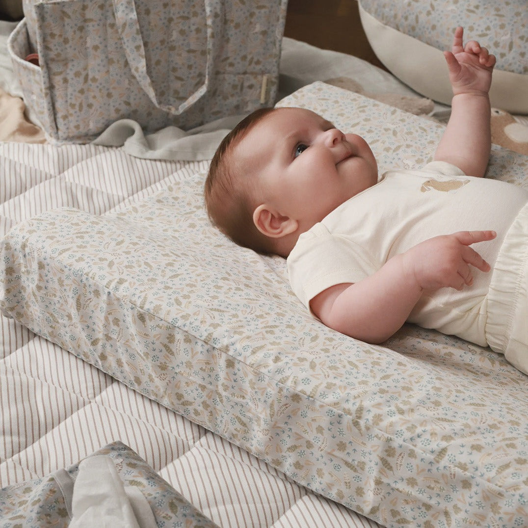 A baby lying on a nature trail changing cushion