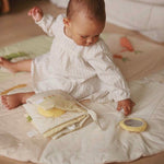 A baby playing with fabric book on activity mat chamomile