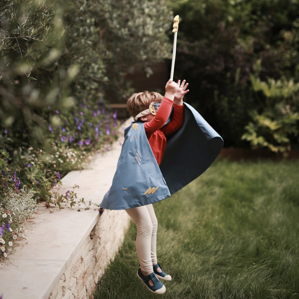 a boy wearing 3 piece superhero dress up set jumping from a wall